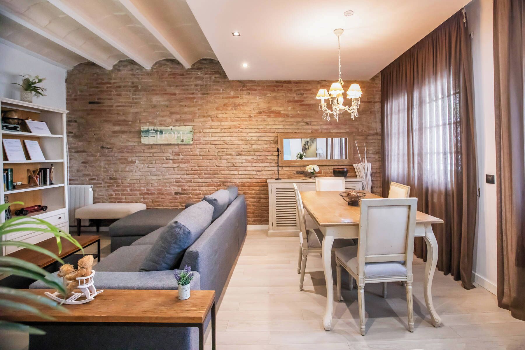 Ein modernes Wohnzimmer mit Backsteinwand, einer Couch, einem Esstisch mit Stühlen und einer Chandelier.