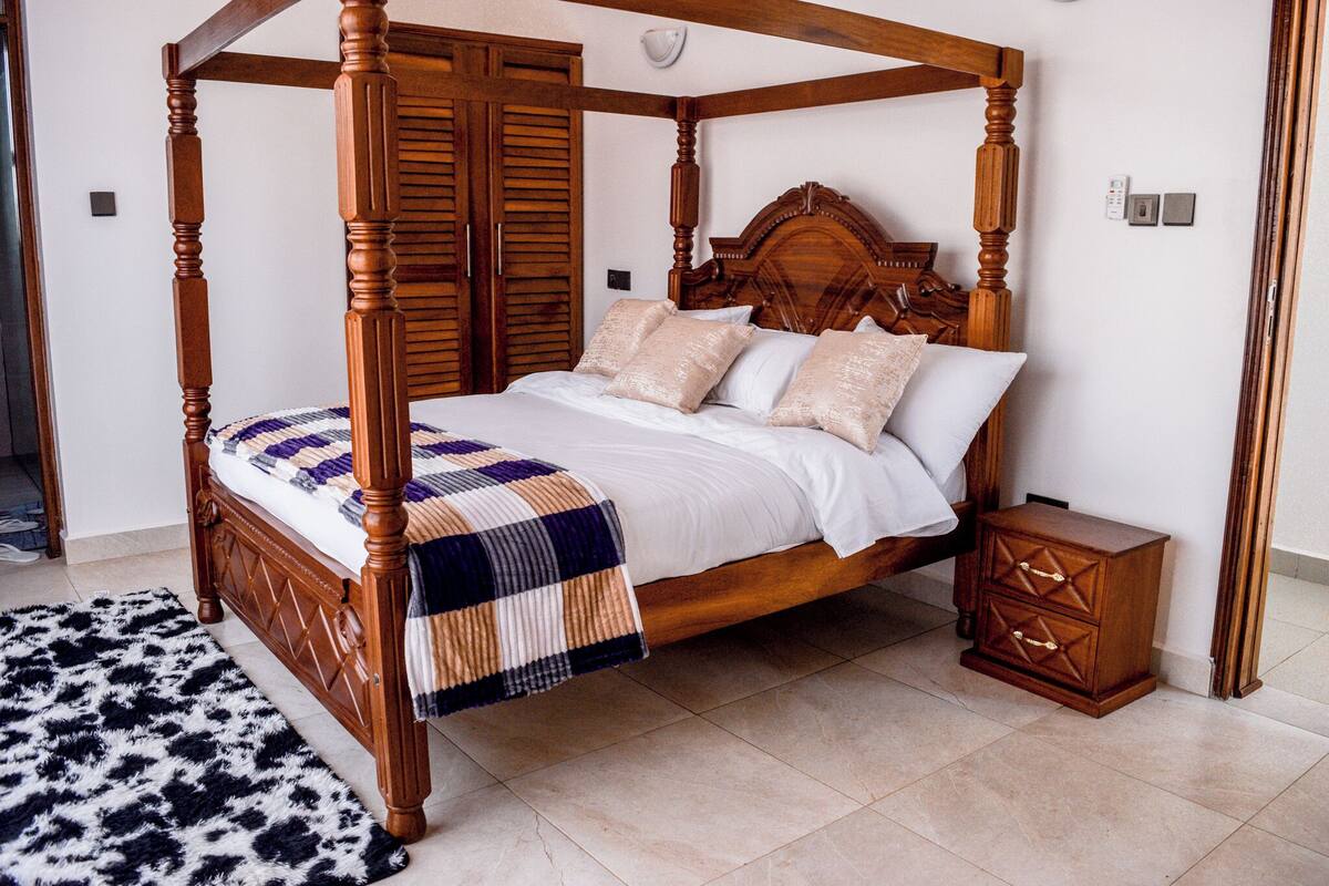 A four-poster bed with a wooden frame, a matching nightstand, and a patterned throw blanket.