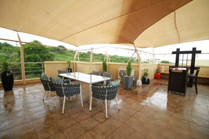 Un patio couvert avec une table et des chaises, des plantes en pot et une vue sur la verdure.