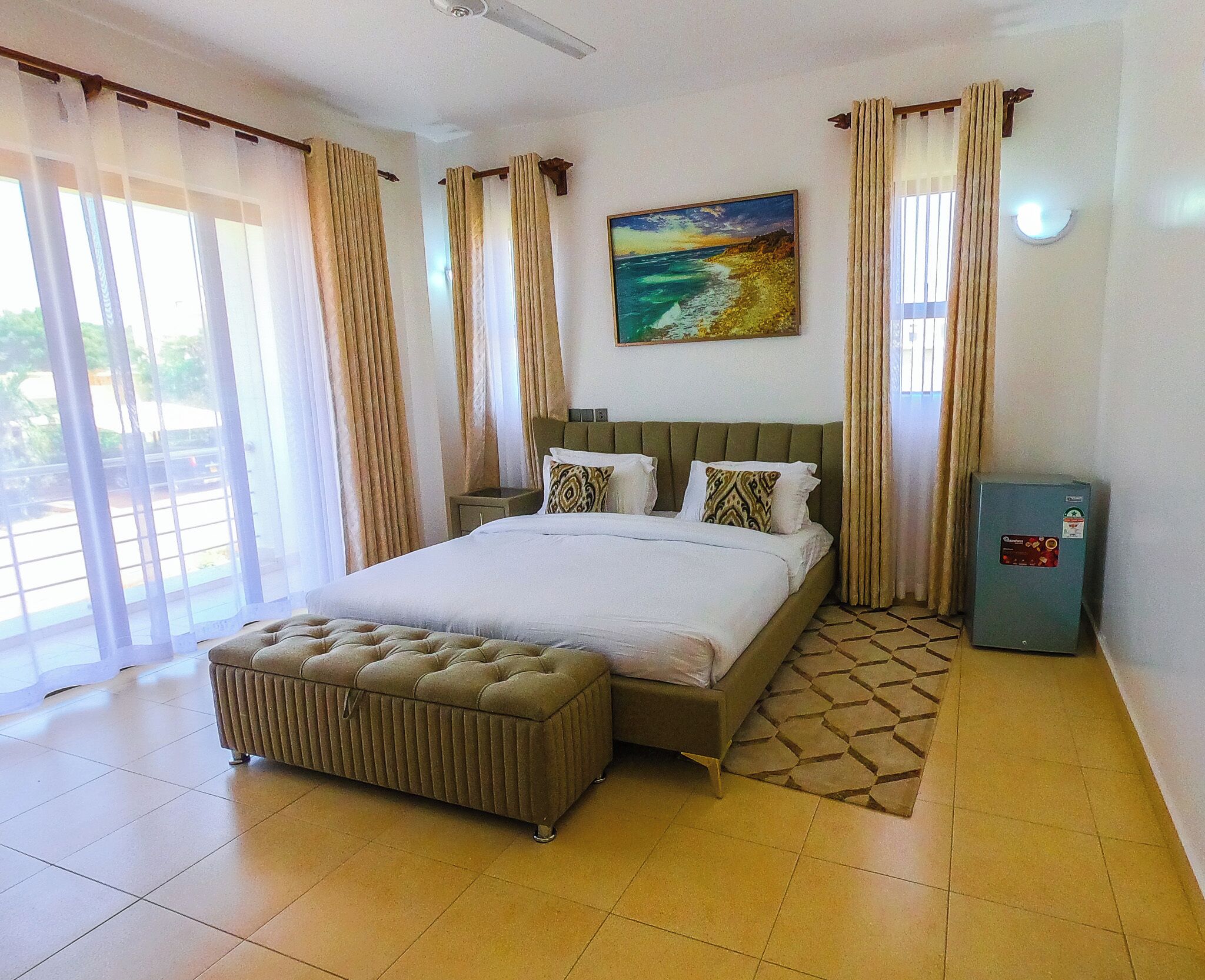 A hotel room with a bed, a nightstand, a bench, a painting, and a power outlet.