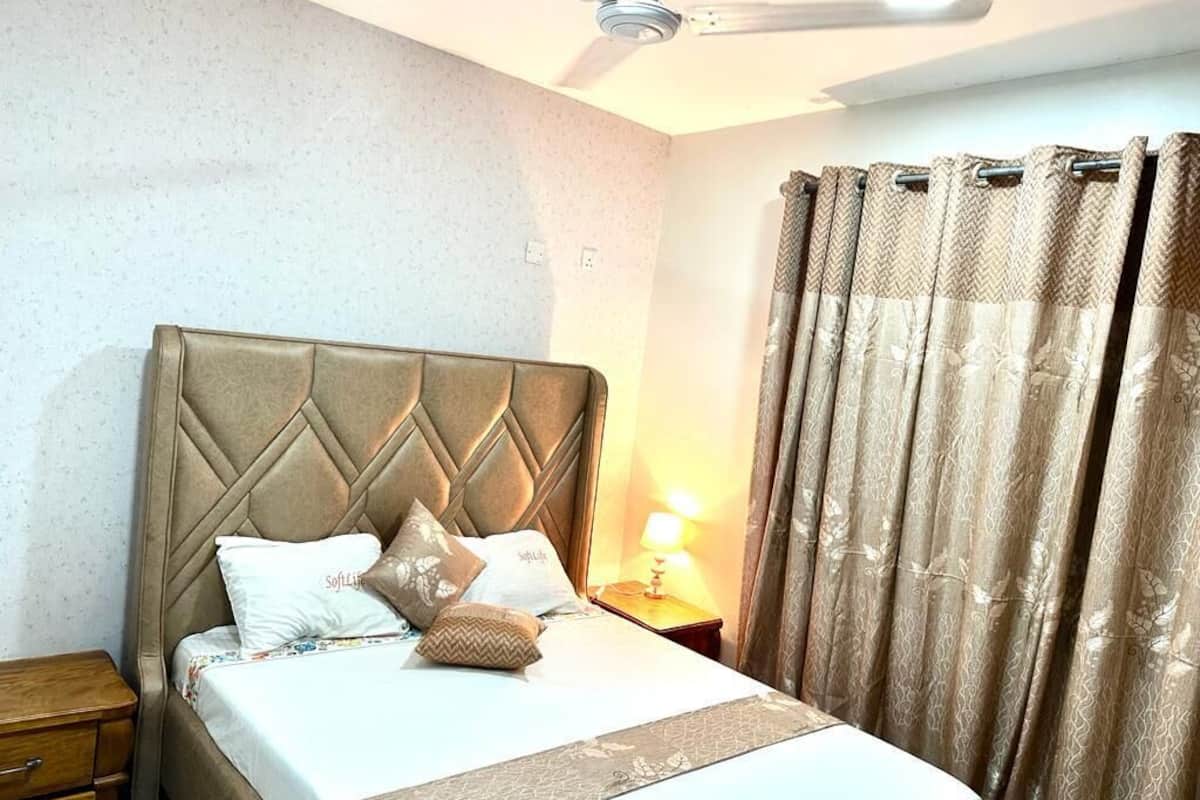 Una cama bien hecha con cabecera, lámpara de noche y mesita de madera.