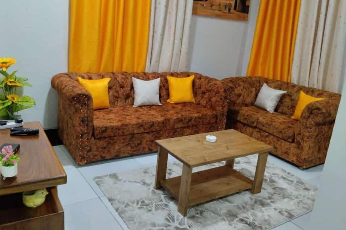 Una sala de estar con un sofá marrón estampado, dos cojines amarillos, una mesa de centro de madera y un cuadro en la pared.