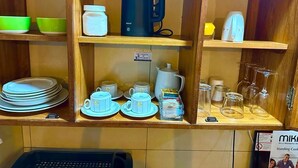 Une étagère en bois contenant divers ustensiles de cuisine, notamment des assiettes, des tasses, une bouilloire et des verres.