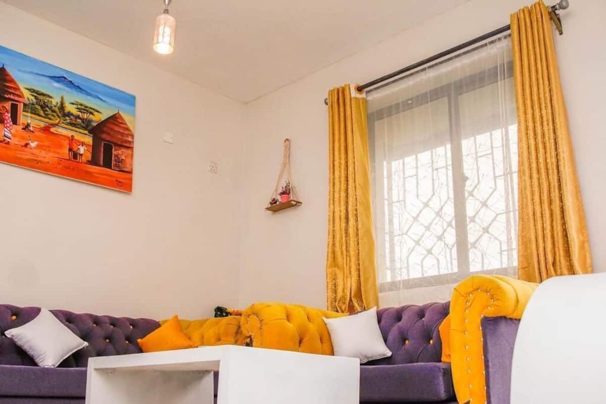 Una sala de estar con un sofá púrpura, una mesita auxiliar blanca y un cuadro en la pared.