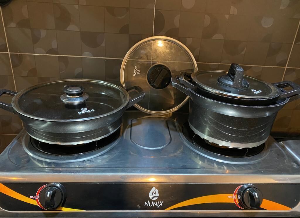 Una cocina con dos ollas sobre la estufa, una tapa en la olla central, y el nombre de marca 'NUNIX' en la estufa.