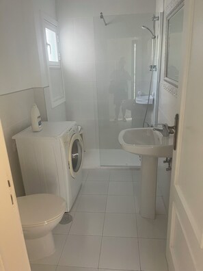 Een kleine, moderne badkamer met toilet, wasmachine, douche en wastafel.