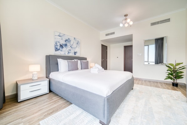 A modern bedroom with a large bed, bedside tables, a wall-mounted mirror, and a ceiling light fixture.