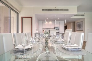 A modern dining area with a glass table set for six, surrounded by white upholstered chairs.