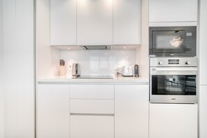 A modern kitchen with white cabinetry, a built-in microwave, and a stainless steel oven.