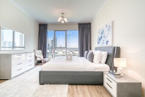 A modern hotel room with a large bed, a desk, a chair, and a view of the cityscape.