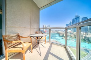 Een balkon met een houten bankje en een tafeltje, met uitzicht op een stadsbeeld met water en moderne gebouwen.