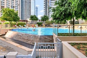 Una piscina en la azotea con una cascada, rodeada de sillones de descanso y follaje, con edificios altos al fondo.
