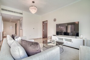 Een moderne woonkamer met een grote flatscreen-tv, een glazen salontafel en een bank met veel kussens.