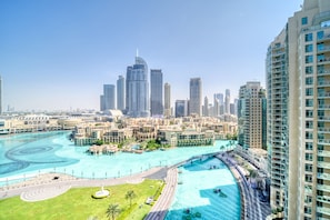 A high-rise hotel with a view of a city skyline, a large swimming pool, and a landscaped area with palm trees.