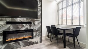 A modern dining area with a fireplace, a flat-screen TV, and a large window with blinds. - House With Modern Interior, Conveniently Located (Manchester)