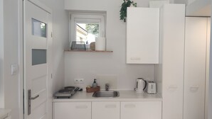 Una cocina compacta con armarios blancos, un lavamanos integrado, una tetera, un tostador y una pequeña ventana sobre el lavamanos.