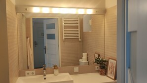 Un baño con lavamanos, espejo, toallero y retrete.