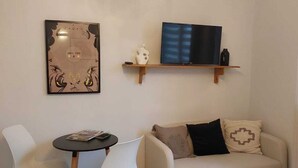 Una sala de estar moderna con un sofá, dos sillones blancos, una mesita, un televisor sobre una estantería de madera y una obra de arte en la pared.