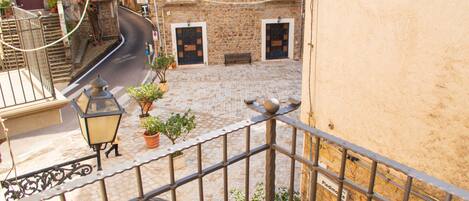 A courtyard with a stone floor, a car, and a building with a stone facade and a balcony.