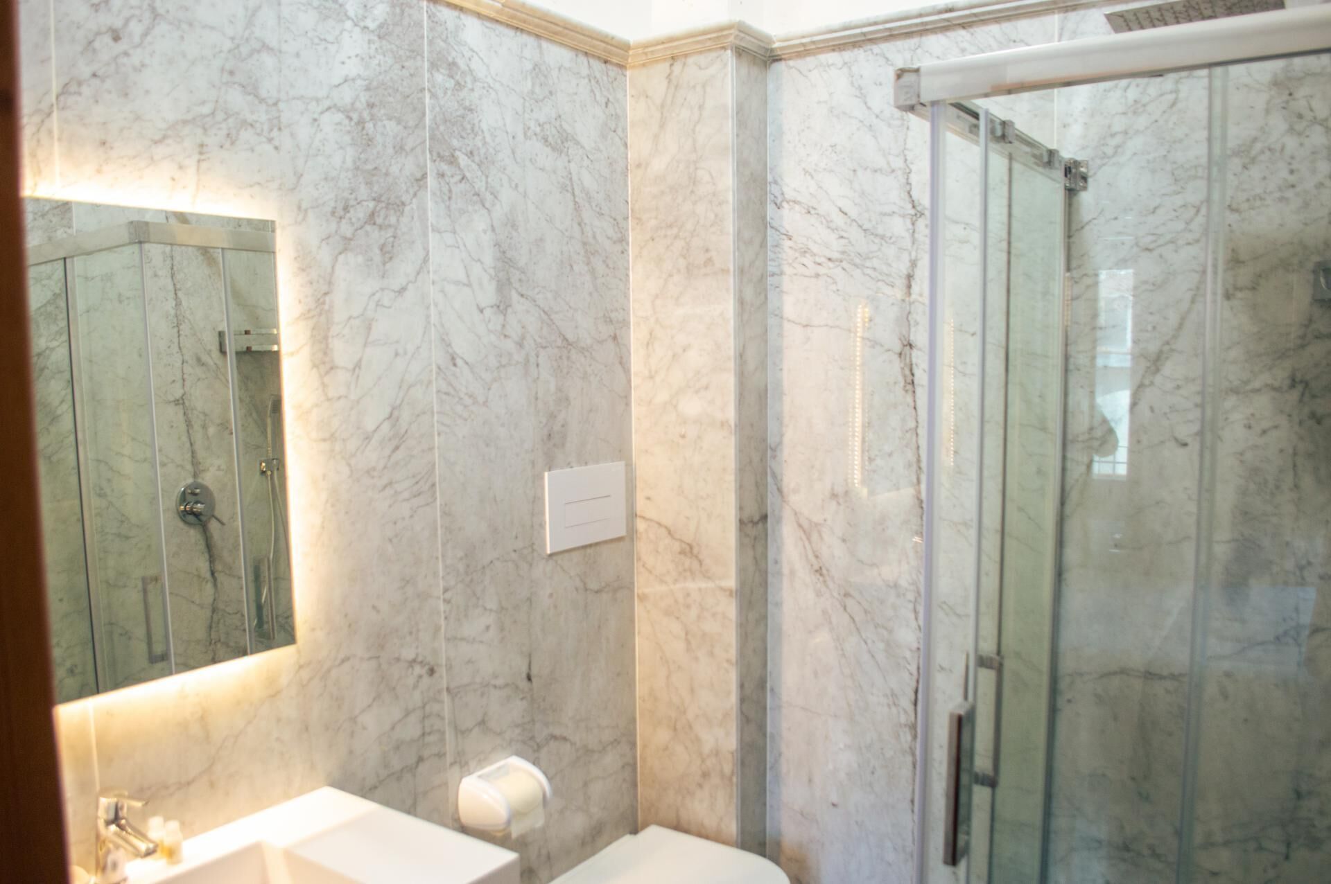 A bathroom with a marble wall, a glass shower enclosure, and a sink with a mirror.