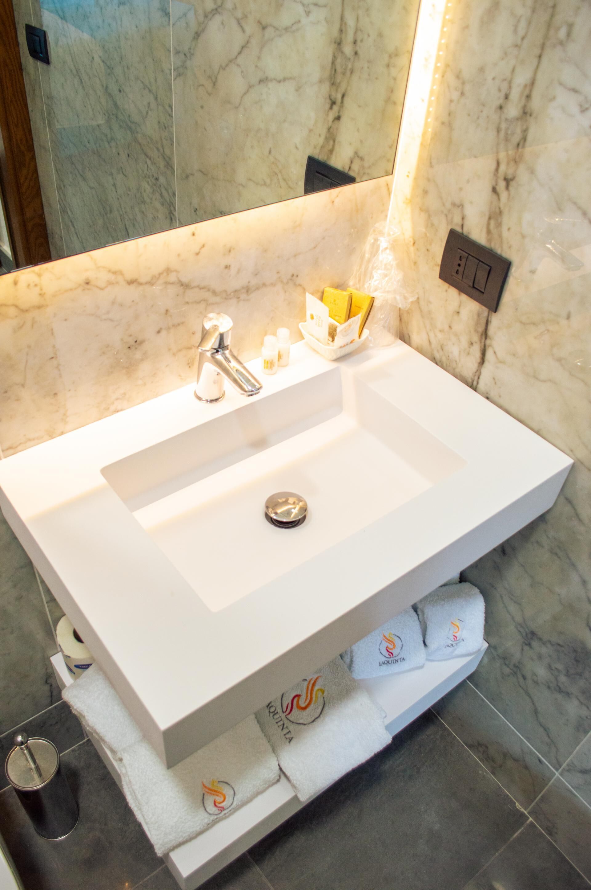 A modern bathroom with a white sink, marble walls, and a mirror.