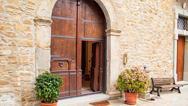 A stone building with a large wooden door, two potted plants, and a bench outside. - Palazzo Iaquinta - Rooms & Restaurant (Cicerale)