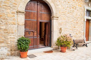 A stone building with a large wooden door, two potted plants, and a bench outside.