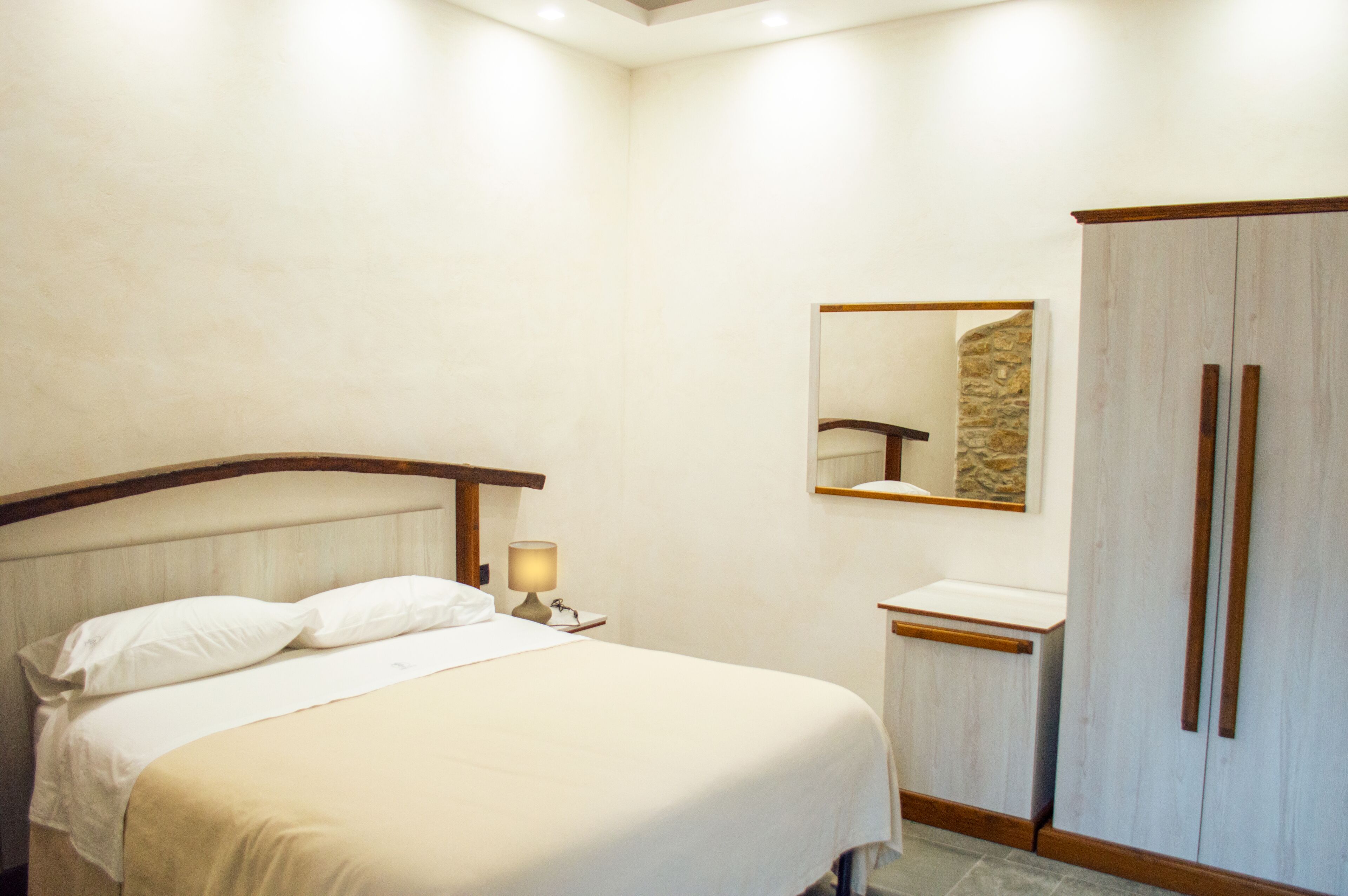 Habitación de hotel con cama, mesita de noche con lámpara, espejo y armario.