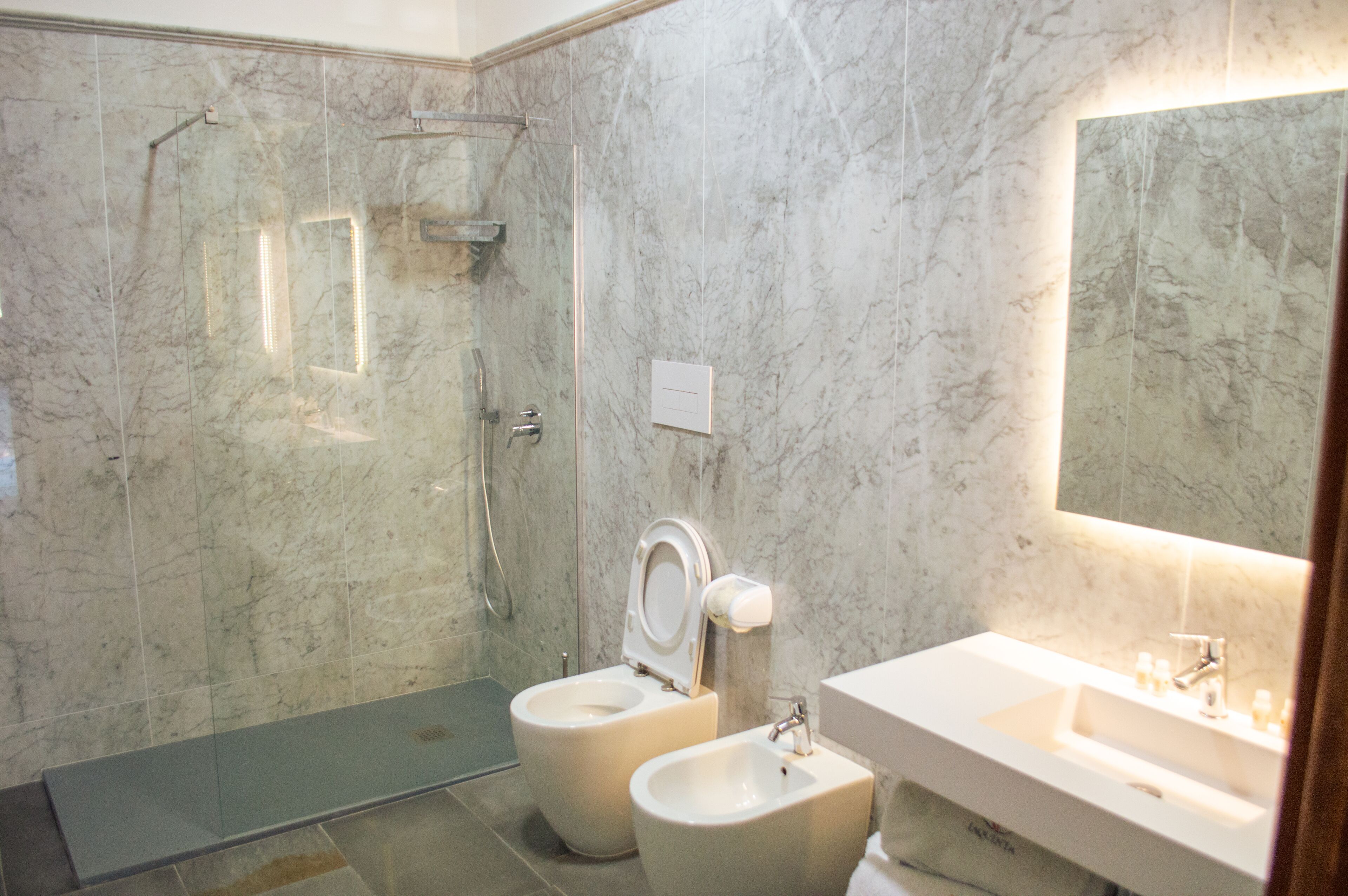 A modern bathroom with a glass shower enclosure, two toilets, and a sink with a mirror.