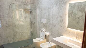 A modern bathroom with a glass shower enclosure, two toilets, and a sink with a mirror.