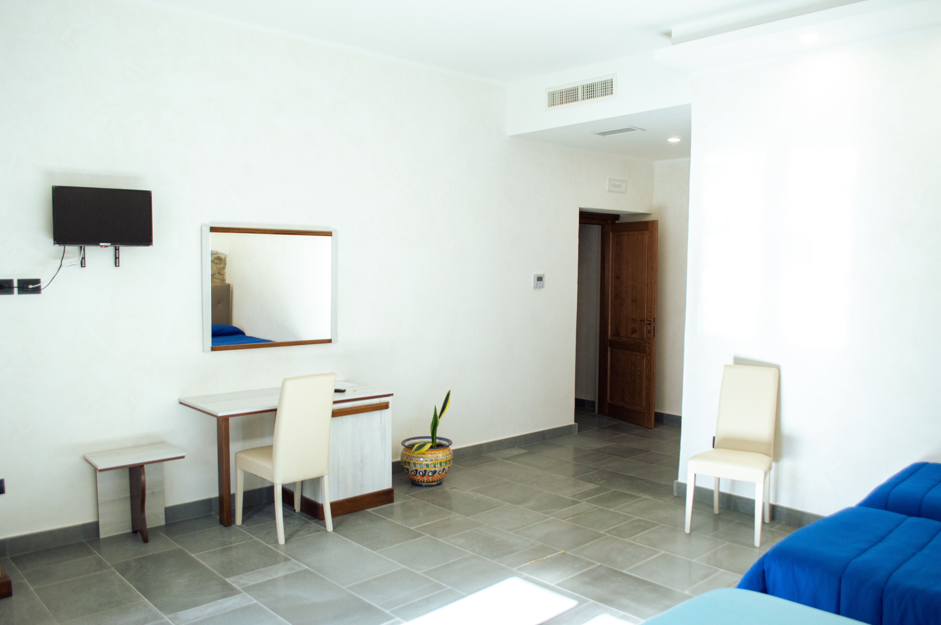 A modern living room with a flat-screen TV, a small table, two chairs, a blue sofa, and a potted plant.