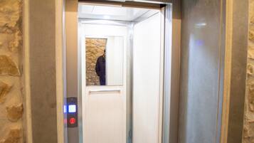 Interior de un ascensor con pared de piedra, una puerta y un panel de control con un botón rojo.