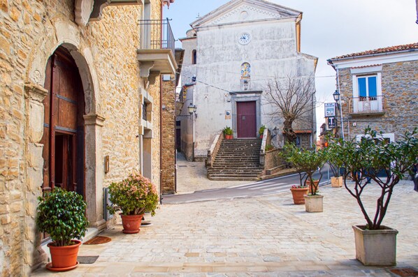 A narrow cobblestone street with stone buildings, a church with a red door, and potted plants along the path.