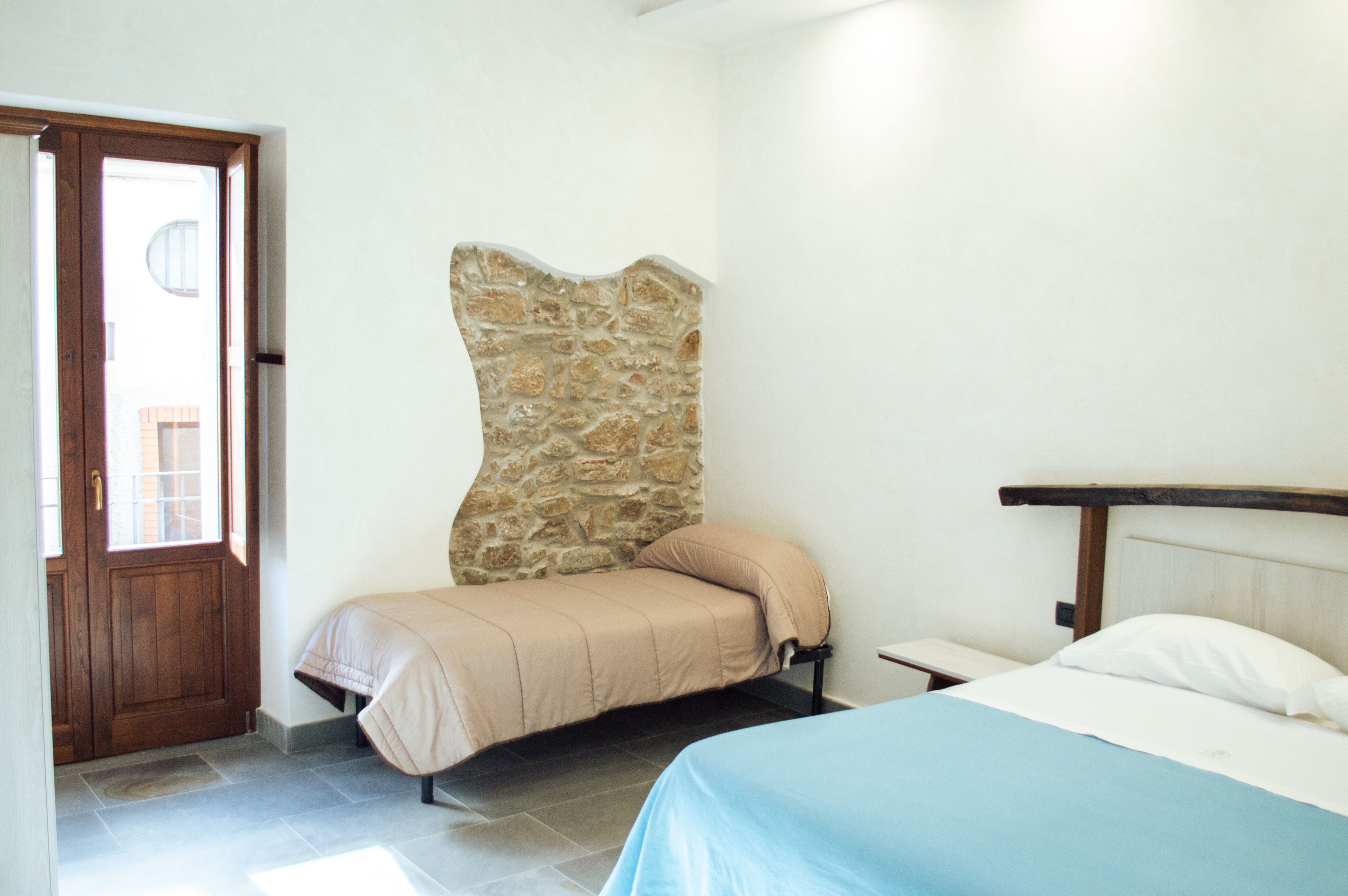 A bedroom with a stone accent wall, a bed with a blue bedspread, and a wooden door.