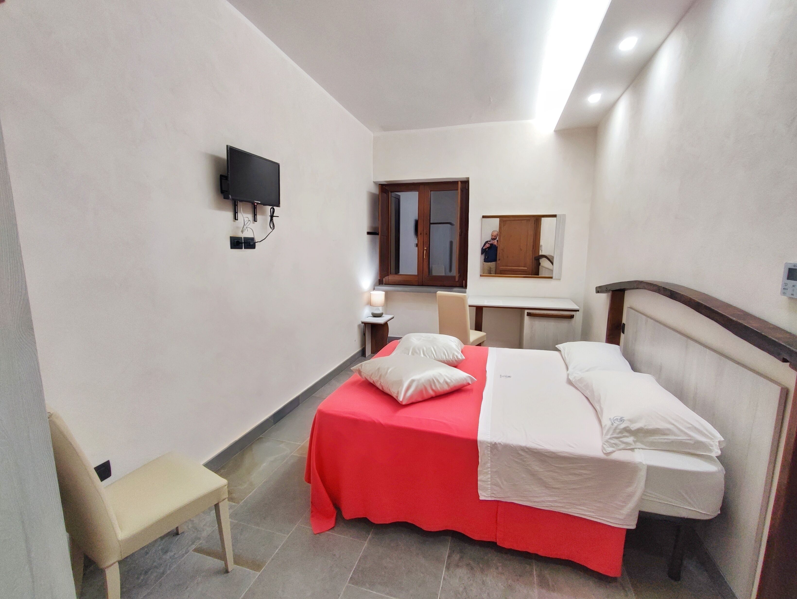 Un dormitorio con cama, mesita de noche, escritorio, silla y televisor montado en la pared.