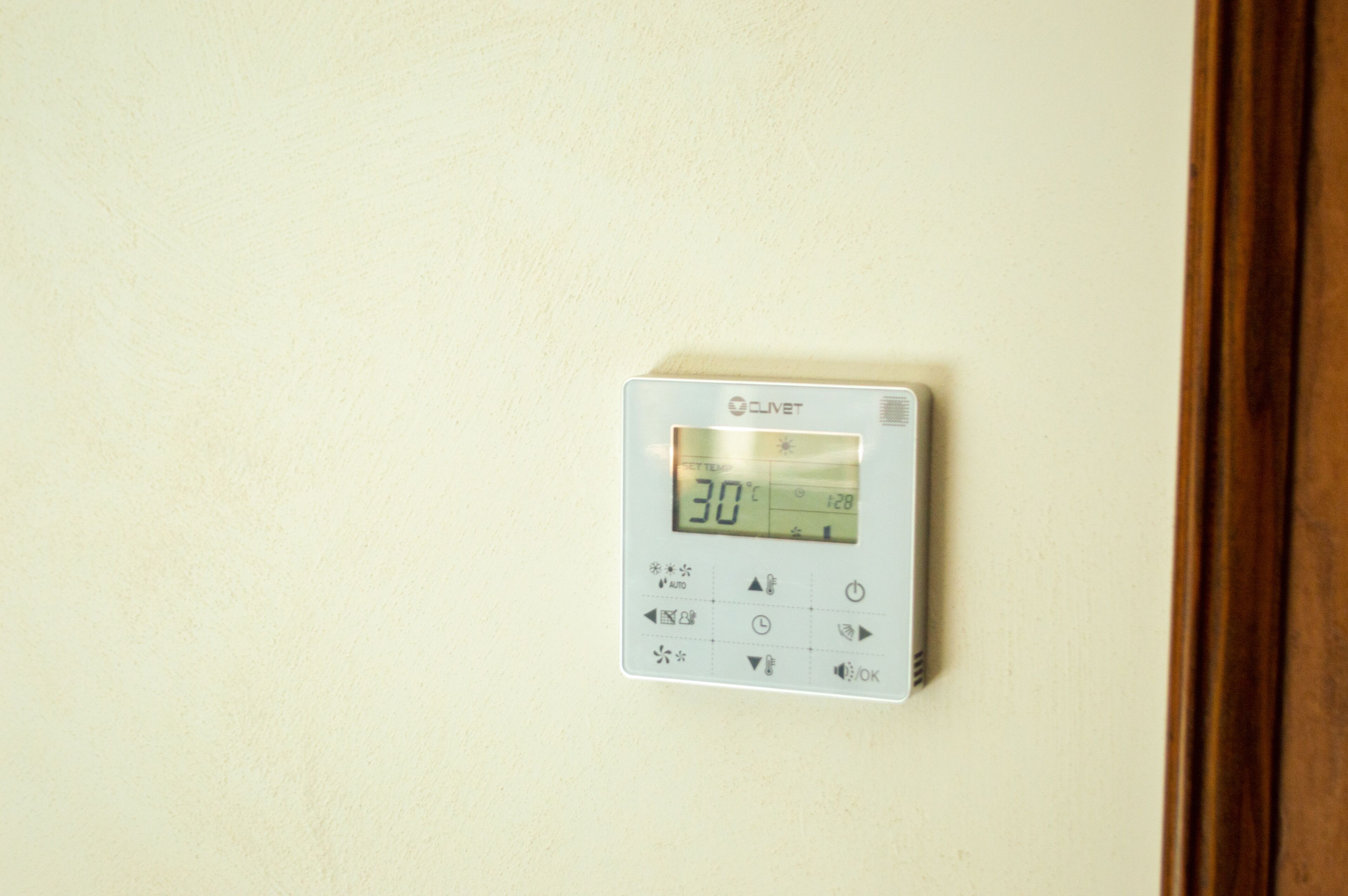 A digital thermostat on a wall displaying a temperature of 30 degrees Celsius.