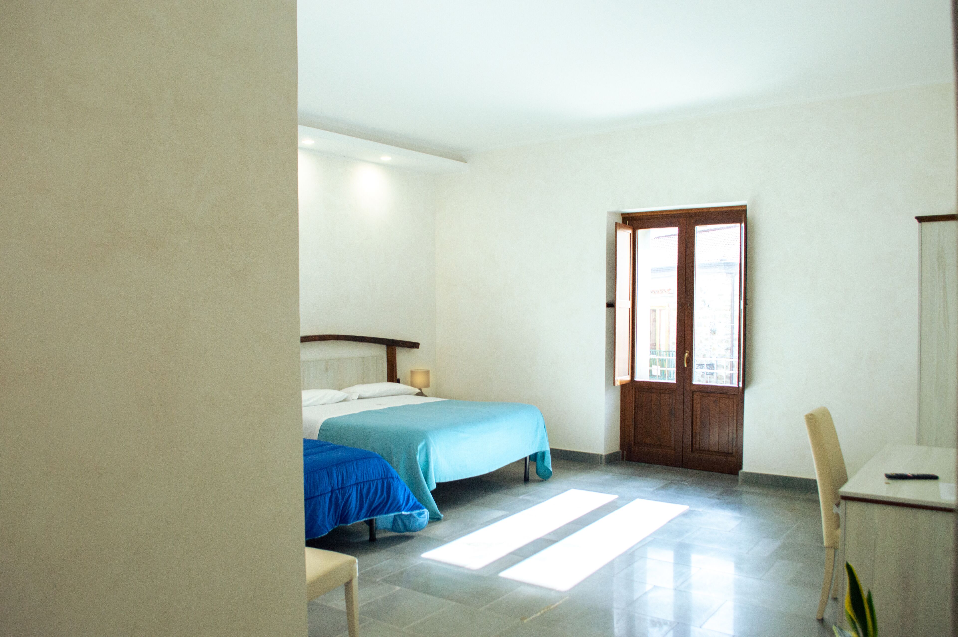 A hotel room with a bed, a desk, and a window.