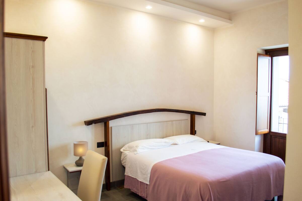 Ein Hotelzimmer mit Bett, Stuhl, Nachttisch und Fenster.