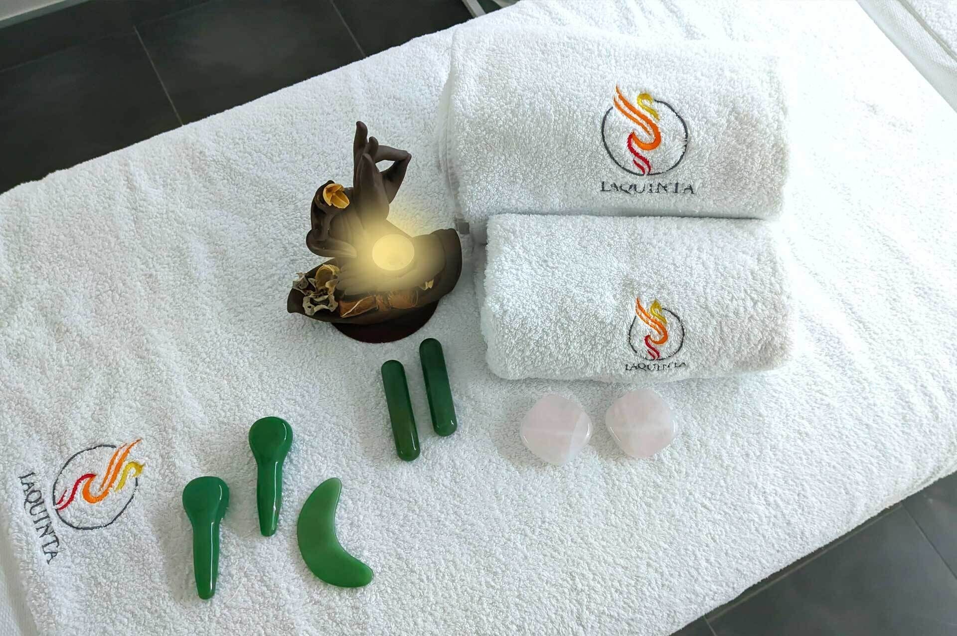 A white towel with a logo and text, green massage tools, and a decorative object on a tiled floor.