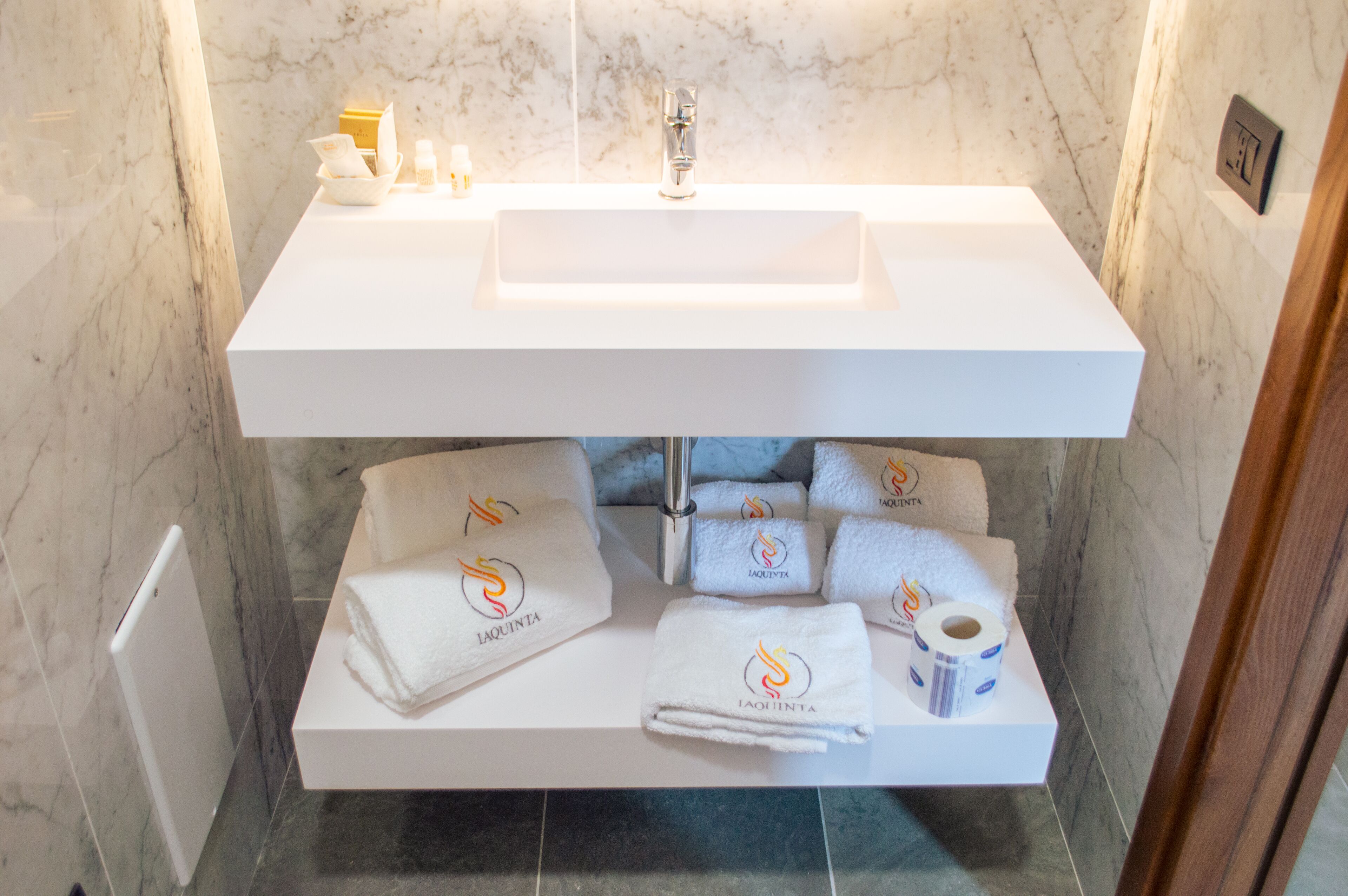 A bathroom with a white sink, marble walls, and a towel rack with towels.