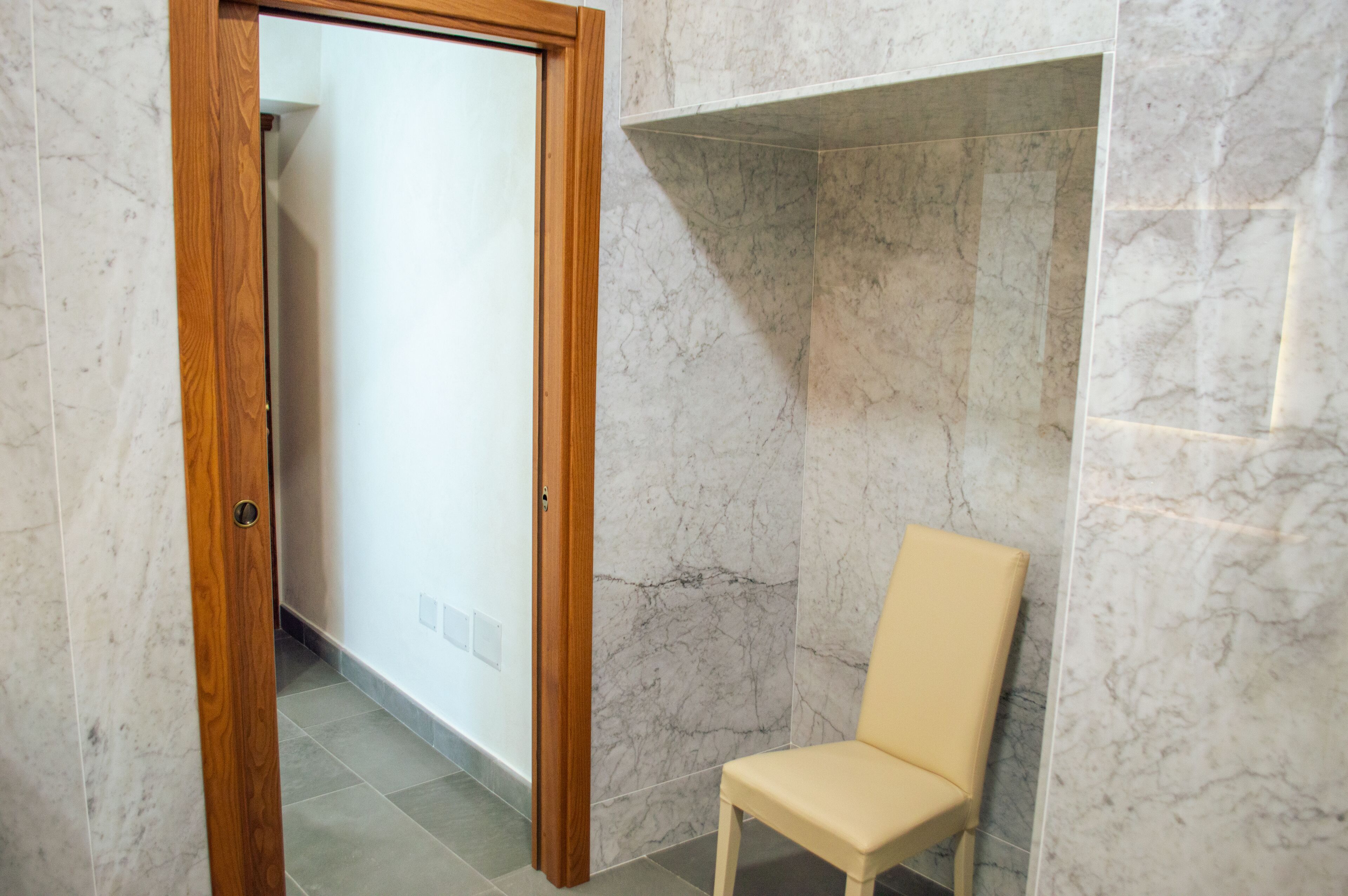Een badkamer met marmeren wanden, een houten deur en een beigekleurige stoel.
