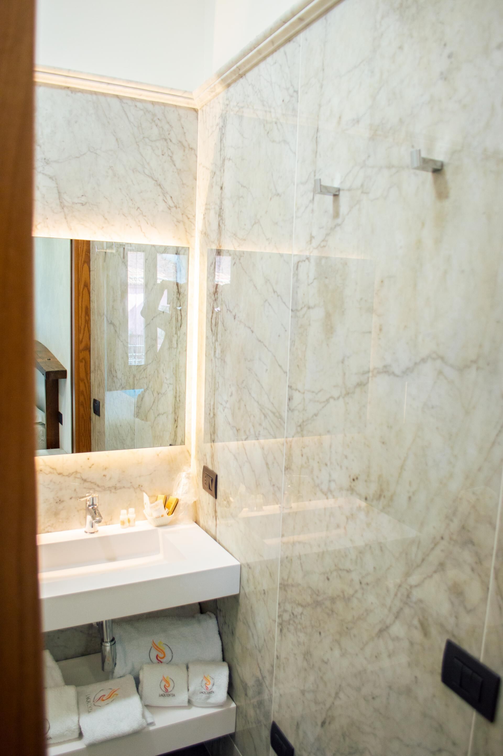 A modern bathroom with a marble sink, a mirror, and a shower area.