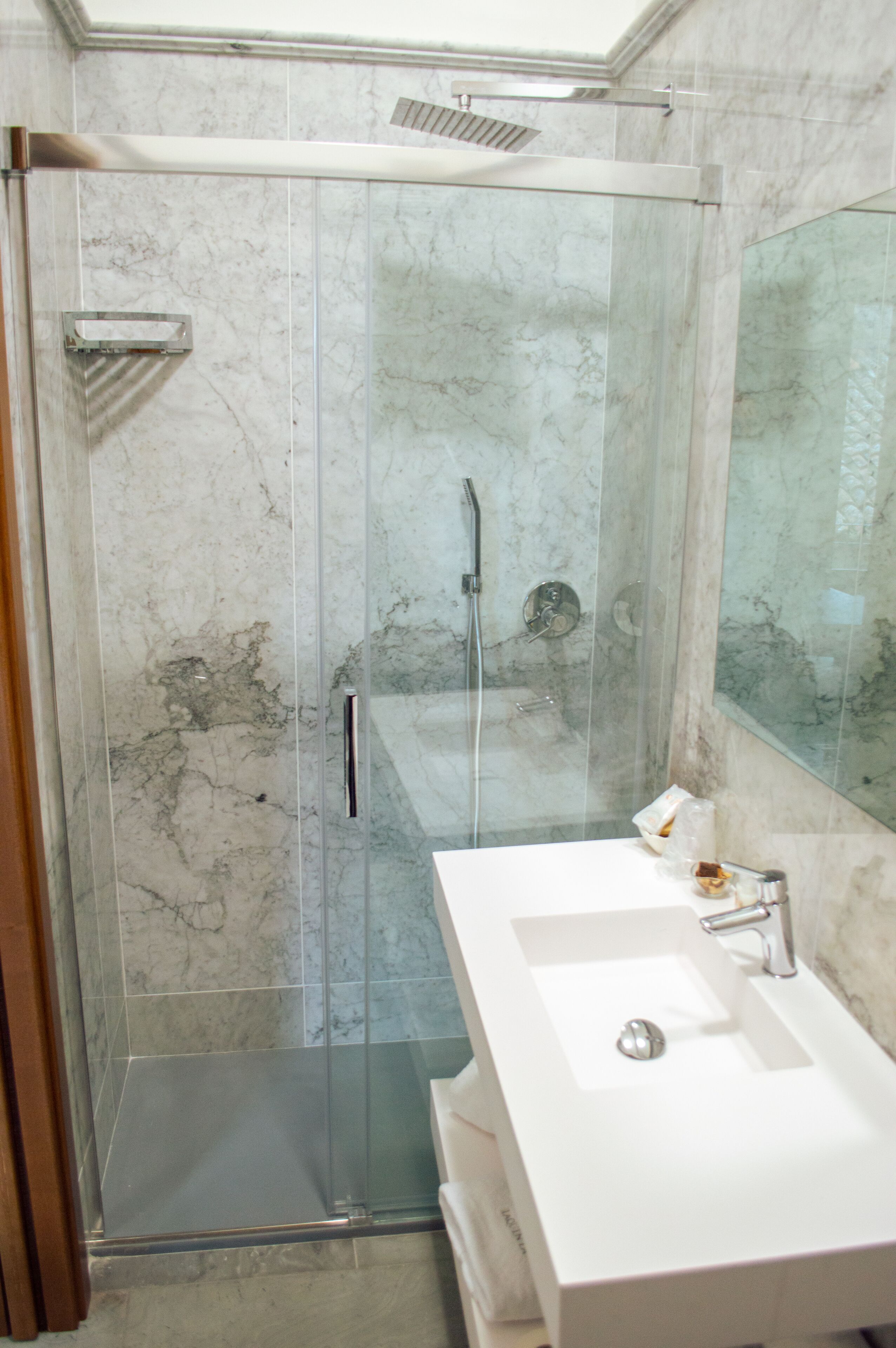 A modern bathroom with a glass-enclosed shower, a white sink, and a large mirror.