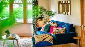 A cozy living room with a blue sofa, patterned cushions, a small side table, and a potted plant. - House - Sleeps up to 9 & Free Parking (Cardiff)