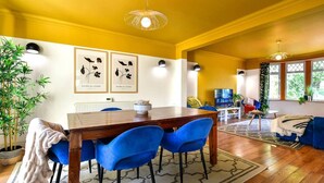 A dining area with a wooden table and blue chairs, a living room with a blue sofa, and a yellow-walled room with a large window. - House - Sleeps up to 9 & Free Parking (Cardiff)