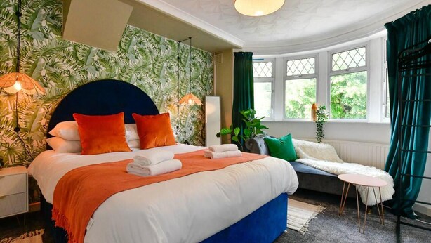 A bedroom with a large bed, a headboard, a bedside table, a small round table, and a window with curtains. - House - Sleeps up to 9 & Free Parking (Cardiff)