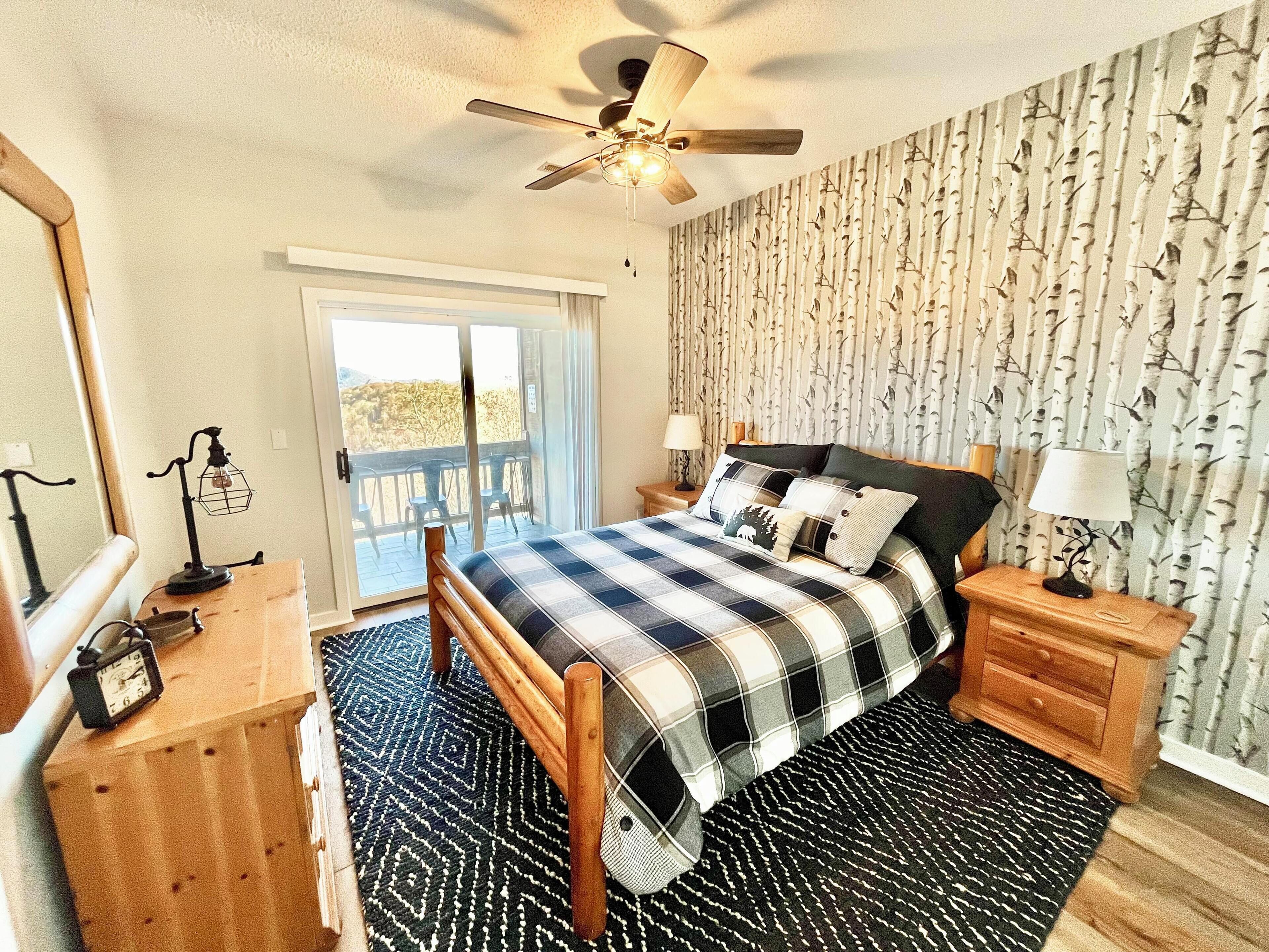 A bedroom with a bed, a ceiling fan, a nightstand with a lamp, a dresser, and a sliding glass door leading to an outdoor area.