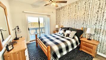 A bedroom with a bed, a ceiling fan, a nightstand with a lamp, a dresser, and a sliding glass door leading to an outdoor area.