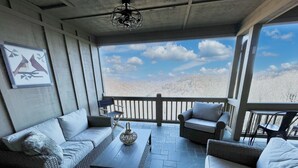 Un patio techado con muebles de mimbre, piso de piedra y vista a un paisaje montañoso.