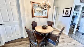 A dining room with a round table, four chairs, a chandelier, a mirror, and a framed picture on the wall.